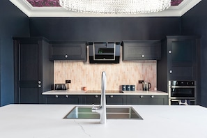 A modern kitchen with dark cabinetry, a marble countertop, a stainless steel sink, a microwave, and a built-in oven. - 2 Bedford House - Close to Town and Seafront (Tenby)
