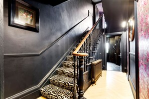 A staircase with patterned carpet and wooden handrails, leading to a room with a radiator and a door with a decorative mirror. - 2 Bedford House - Close to Town and Seafront (Tenby)