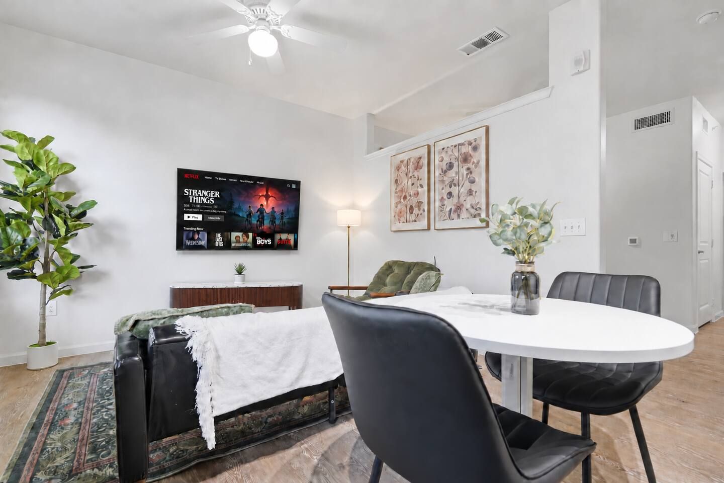 Un salon moderne avec un téléviseur à écran plat, une table à manger avec des chaises, un canapé, une plante et des œuvres d’art accrochées au mur.