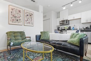 A living room with a green sofa, a black leather sofa, and a glass coffee table. - The Austin Haven | Stylish 1Bed + Pool&Gym (Pflugerville)