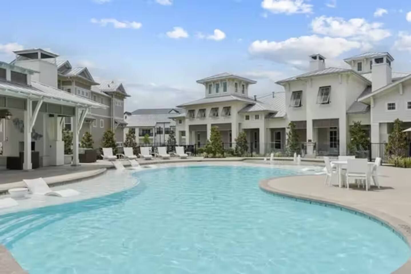 Una piscina rodeada de edificios blancos con varios balcones y un cielo despejado.