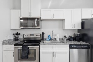 A modern kitchen with stainless steel appliances, white cabinetry, and granite countertops. - The Austin Haven | Stylish 1Bed + Pool&Gym (Pflugerville)