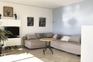 Ein modernes Wohnzimmer mit einem Ecksofa, einem kleinen runden Tisch, einem Flachbildfernseher und zwei Bildern an der Wand.