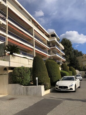 A multi-story residential building with balconies, a parking area, and neatly trimmed bushes. - Akwaba 1-Bedroom Apartment with Ocean View, Terrace, and Pool (Cassis)