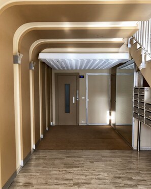 Ein Korridor mit Teppichboden, einer Tür mit vertikalem Griff und einer Treppe mit Metallgeländern.