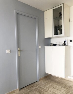 Ein Zimmer mit geschlossener Tür, einem weißen Schrank mit Glastür und einem kleinen Regal mit Gegenständen.