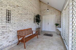 A brick wall, a wooden bench, a white door, and a potted plant. - SB Spring Getaway w/ Pool • Near I-45 • Sleeps 10 (Spring)