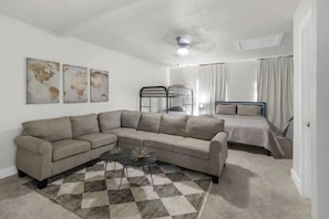 A living room with a sofa, a coffee table, and a bunk bed in the background. - SB Spring Getaway w/ Pool • Near I-45 • Sleeps 10 (Spring)