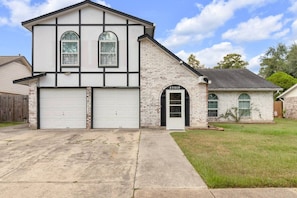 A two-story house with a garage, a brick exterior, and a number '23910' on the front door. - SB Spring Getaway w/ Pool • Near I-45 • Sleeps 10 (Spring)