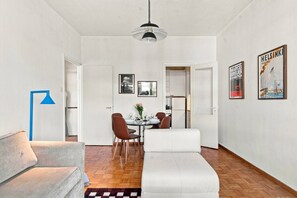 A modern living room with a sofa, a dining table with chairs, and a kitchen area in the background. - Timeless Nordic | Quiet Street | Parquet | Lift (Helsinki)
