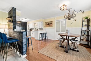 A modern kitchen with white cabinets, a built-in stove, and a dining area with a round table and bar stools. - Dave’s Place (Bentonville)