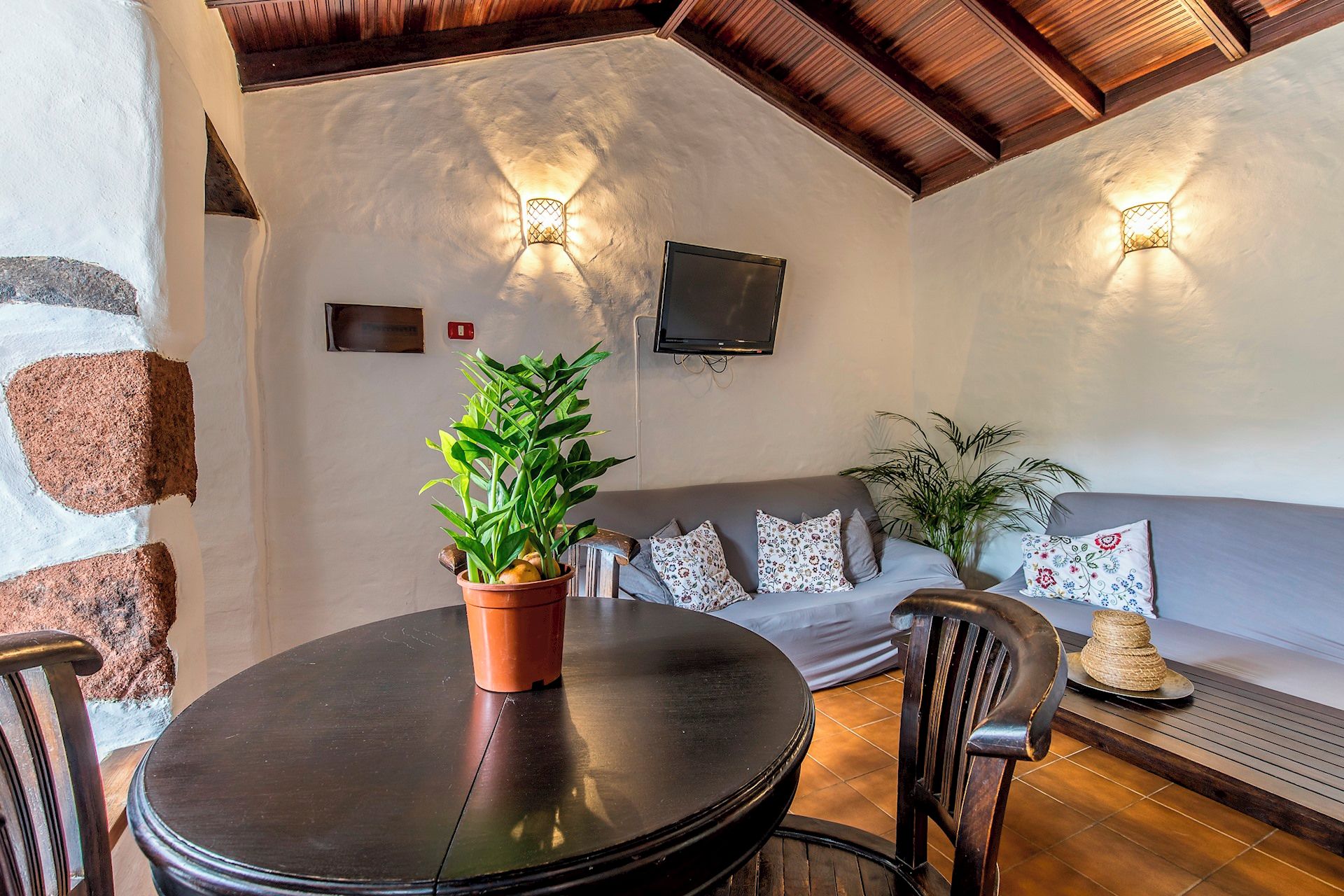 Un salon chaleureux avec une table ronde, un canapé agrémenté de coussins à motifs et une plante en pot.