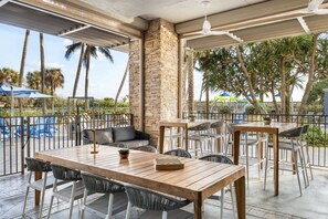 An outdoor patio with tables and chairs, a stone pillar, and a view of palm trees. - Ocean View- Amazing 2 Bedroom Villa- Marriott's Oceana Palms- Full Resort Access (Riviera Beach)