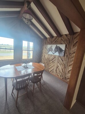 Ein Essbereich mit Holztisch und -stühlen, einem Gemälde von Pferden an der Wand und Blick ins Freie durch ein Fenster.