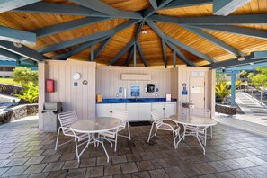 An outdoor seating area with a covered roof, a clock, and a sign indicating a shower. - Kona Reef#a1: Sand & Surf Beachfront Corner! (Kailua-Kona)
