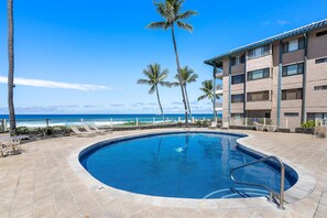 A swimming pool with a view of the ocean, palm trees, and a building with multiple windows. - Kona Reef#a1: Sand & Surf Beachfront Corner! (Kailua-Kona)