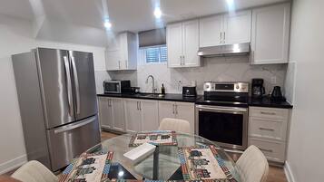 Una cocina funcional con electrodomésticos de acero inoxidable, una mesa de vidrio y armarios blancos.