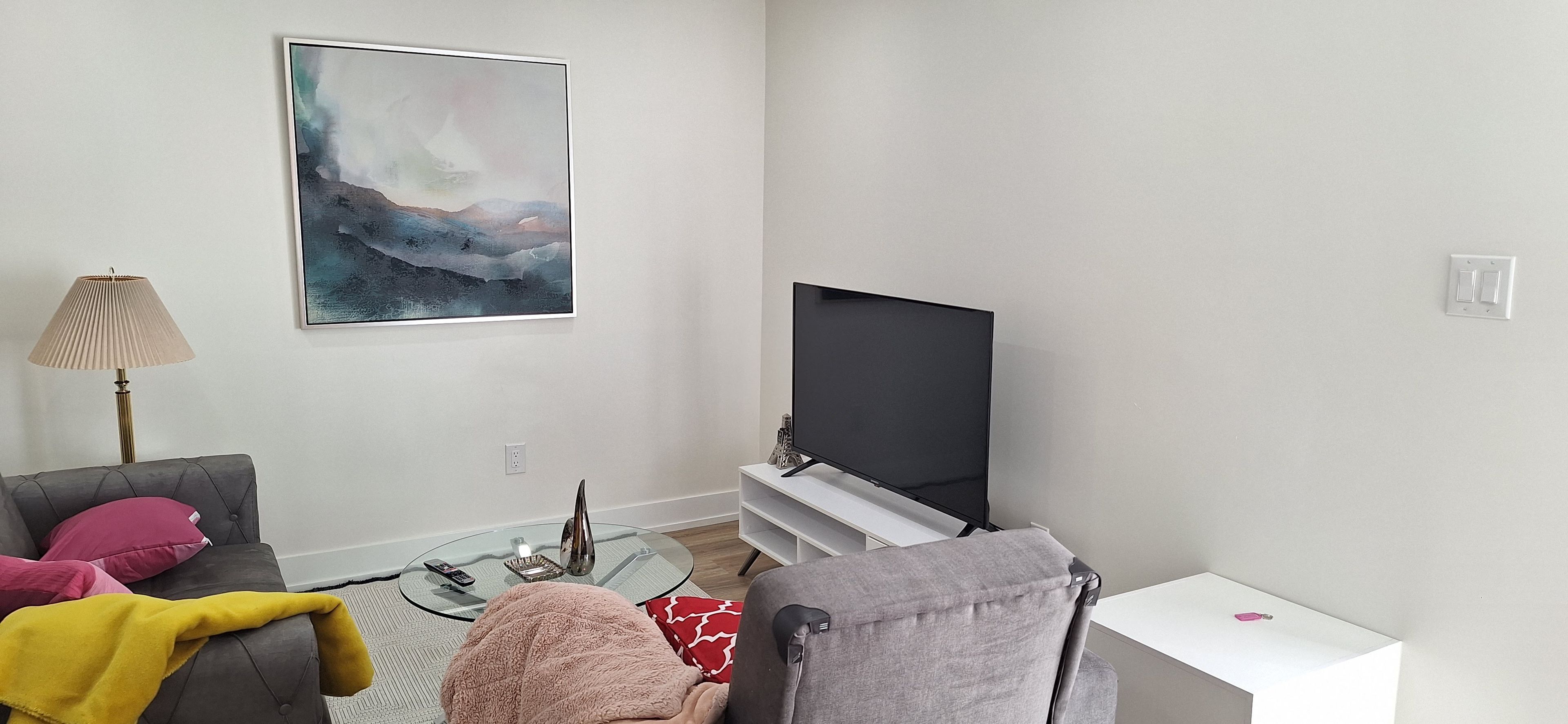 A living room with a flat-screen TV, a sofa, a coffee table, and a lamp.