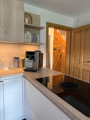 A modern kitchen with a built-in stove, a coffee machine, and wooden cabinets.