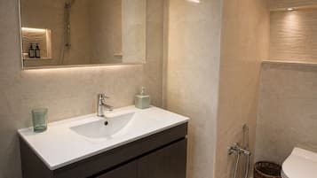 A modern bathroom with a white sink, dark cabinets, a mirror, and a shower.