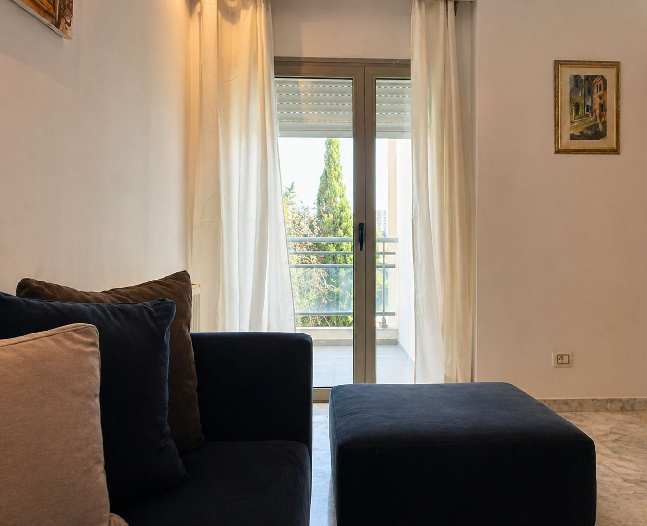 A living room with a sofa, ottoman, and a balcony with a view.