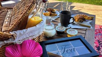 Desayuno con croissants, jugo y té en una mesa al aire libre.