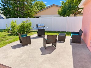 An outdoor patio with a grill, wicker furniture, and a white fence. - Pink Palace - Stylish Sarasota Getaway with Spacious Rooms & Smart TVs (Sarasota)