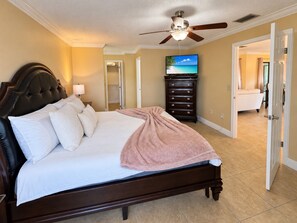 A bedroom with a bed, a ceiling fan, a dresser, and a television. - Pink Palace - Stylish Sarasota Getaway with Spacious Rooms & Smart TVs (Sarasota)