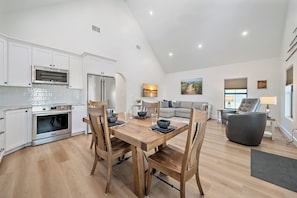 A modern kitchen with white cabinets, stainless steel appliances, and a dining area with a wooden table and chairs. - Pinecraft Pearl | Heart of Pinecraft + Rocking Chairs (Sarasota)