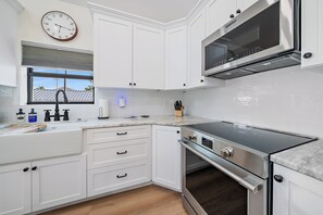 A modern kitchen with white cabinetry, a stainless steel stove, and a window with blinds. - Pinecraft Pearl | Heart of Pinecraft + Rocking Chairs (Sarasota)