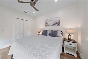 A bedroom with a bed, nightstands, a ceiling fan, a painting, and a white wardrobe. - Pinecraft Pearl | Heart of Pinecraft + Rocking Chairs (Sarasota)