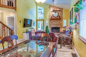 A cozy living room with a fireplace, a dining area with a glass-top table, and a staircase leading to an upper level. - Tuscany at Shaver Lake -3BR Mountain Escape (Shaver Lake)