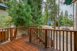 Une terrasse en bois avec une rambarde en métal, entourée d’arbres et bordée d’un quartier résidentiel.