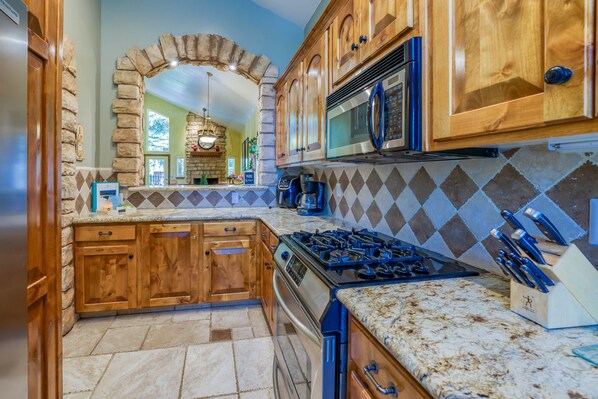 Une cuisine avec des meubles de rangement en bois, une arche en pierre, une cuisinière à gaz et un four à micro-ondes.