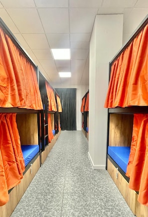 A corridor with bunk beds, each with a blue mattress and orange curtains. - UWANT HOSTEL UP (Sant Vicent del Raspeig)