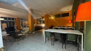 A room with a long table, chairs, a sofa, and a window. - UWANT HOSTEL UP (San Vicente del Raspeig)