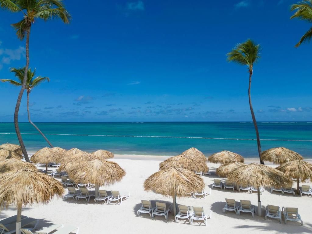 Une plage de sable blanc, avec des parasols en chaume et des chaises longues.