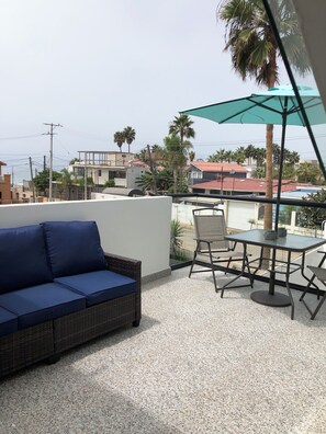 A balcony with a blue sofa, a table with chairs, and a green umbrella. - Marvelous 4-bedroom house in Playas de Rosarito perfect for families. (Playas de Rosarito)