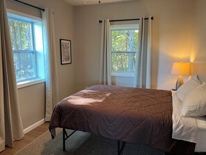 A bedroom with a bed, a window with curtains, a bedside lamp, and a framed picture on the wall.