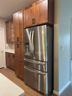 A stainless steel Whirlpool refrigerator with a double door, built-in ice maker, and a freezer drawer, situated in a kitchen with wooden cabinets and a white countertop.