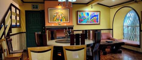 A dining area with a round table, chairs, a chandelier, and artwork on the walls.