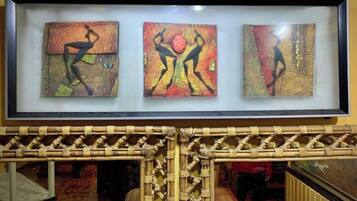 A framed artwork with three panels depicting abstract figures in dynamic poses, displayed above a woven bamboo structure.