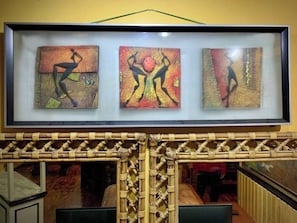 A framed artwork with three panels depicting abstract figures in dynamic poses, displayed above a woven bamboo structure. - Cozy Escape in Baguio (Baguio)