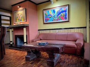 A room with a leather sofa, a wooden coffee table, a fireplace, and two framed artworks on the walls. - Cozy Escape in Baguio (Baguio)