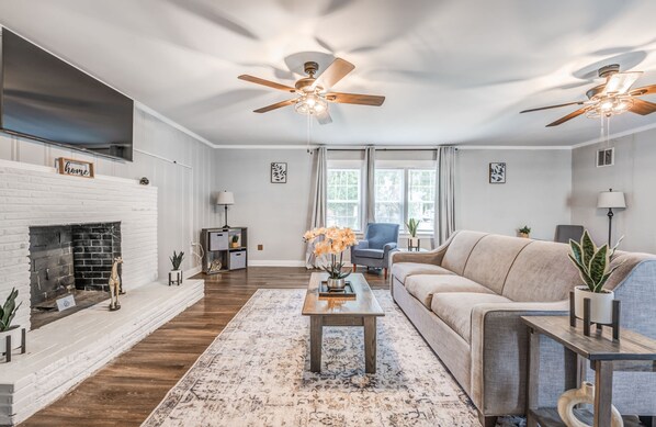 A living room with a fireplace, a sofa, a coffee table, and two ceiling fans. - Mins to Airport & Dining- Wonderful in Whitehaven (Memphis)