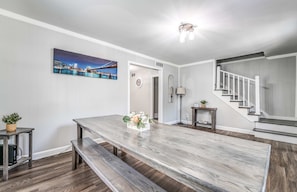 A modern interior with a wooden dining table, bench seating, a staircase, and a cityscape painting on the wall. - Mins to Airport & Dining- Wonderful in Whitehaven (Memphis)