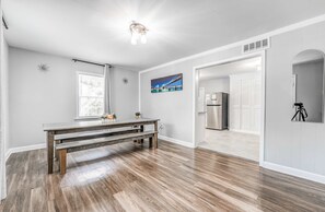 Une pièce spacieuse avec un plancher en bois, une table à manger, un réfrigérateur et une grande fenêtre équipée de stores.