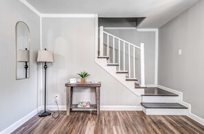 Un intérieur moderne avec un plancher en bois, un escalier blanc, une petite table avec une plante et une lampe.