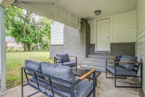 Ein überdachter Patio-Bereich mit Kamin, Sitzgelegenheiten im Freien und Blick auf ein Wohnhaus.