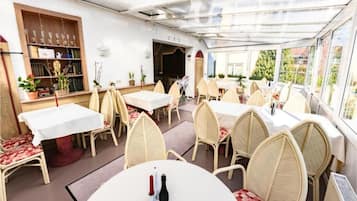 Un espacio de comedor al aire libre con mesas y sillas, una estantería con trofeos y plantas en macetas.